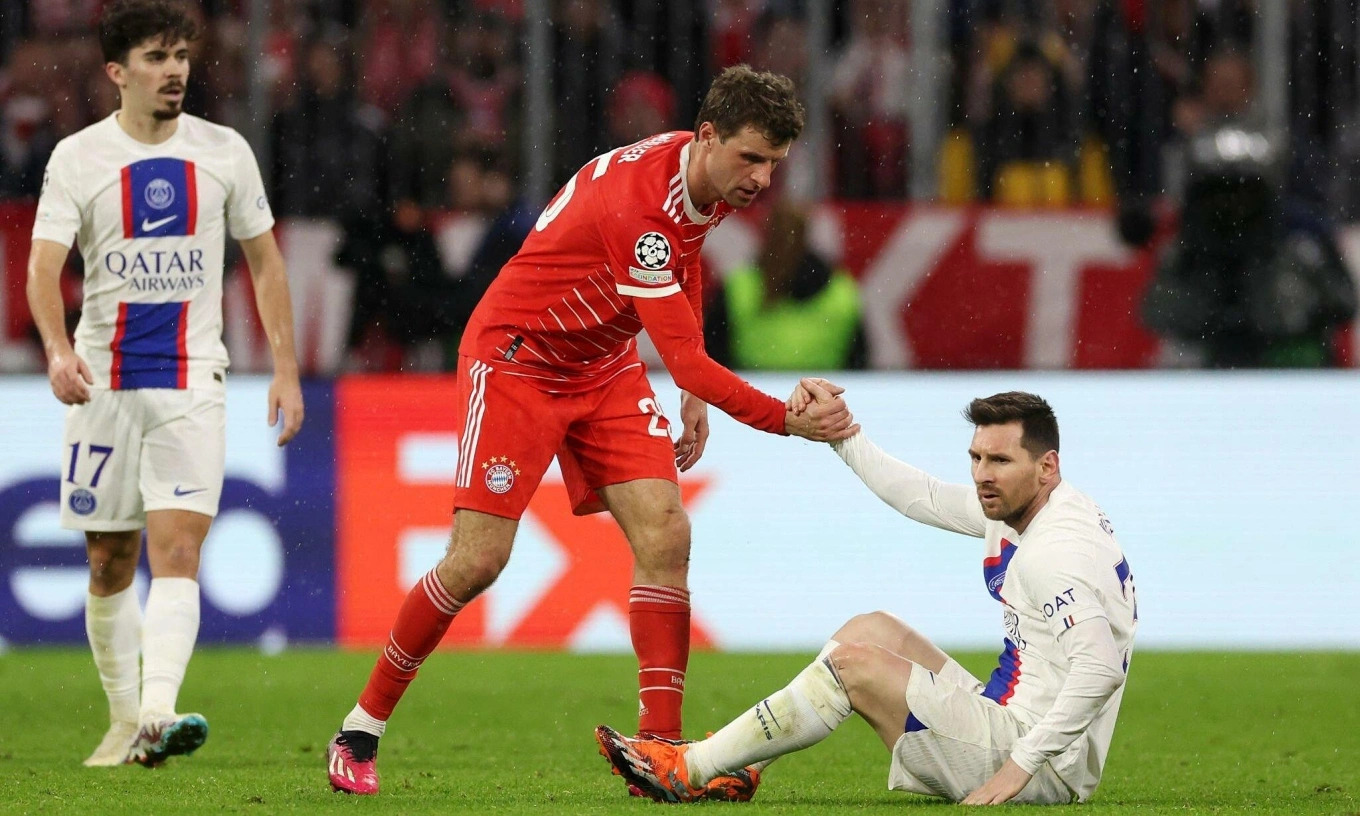 Lionel Messi sitting on the pitch in a PSG kit while Bayern Munich captain Thomas Muller stands nearby during their 2023 Champions League meeting, illustrating their rivalry ahead of Messi vs Muller MLS Cup 2025 coverage.
